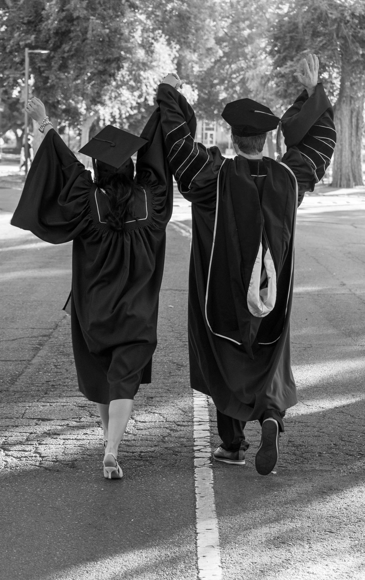 Black-and-white portrait of two graduates in caps and gowns walking arm-in-arm — UC Davis graduation photographer