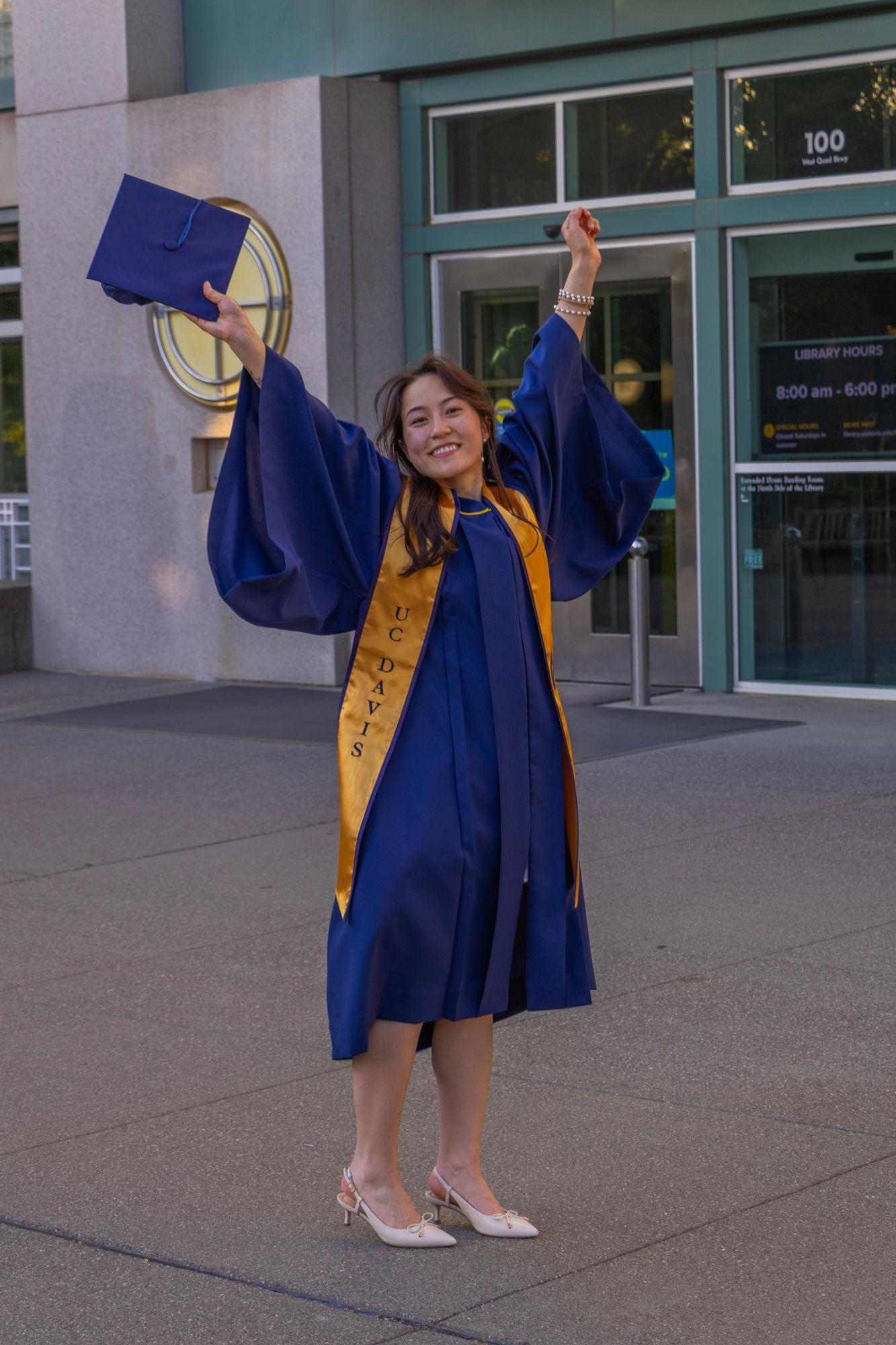 UC Davis graduate celebrating with cap raised outside the library — Davis graduation photographer