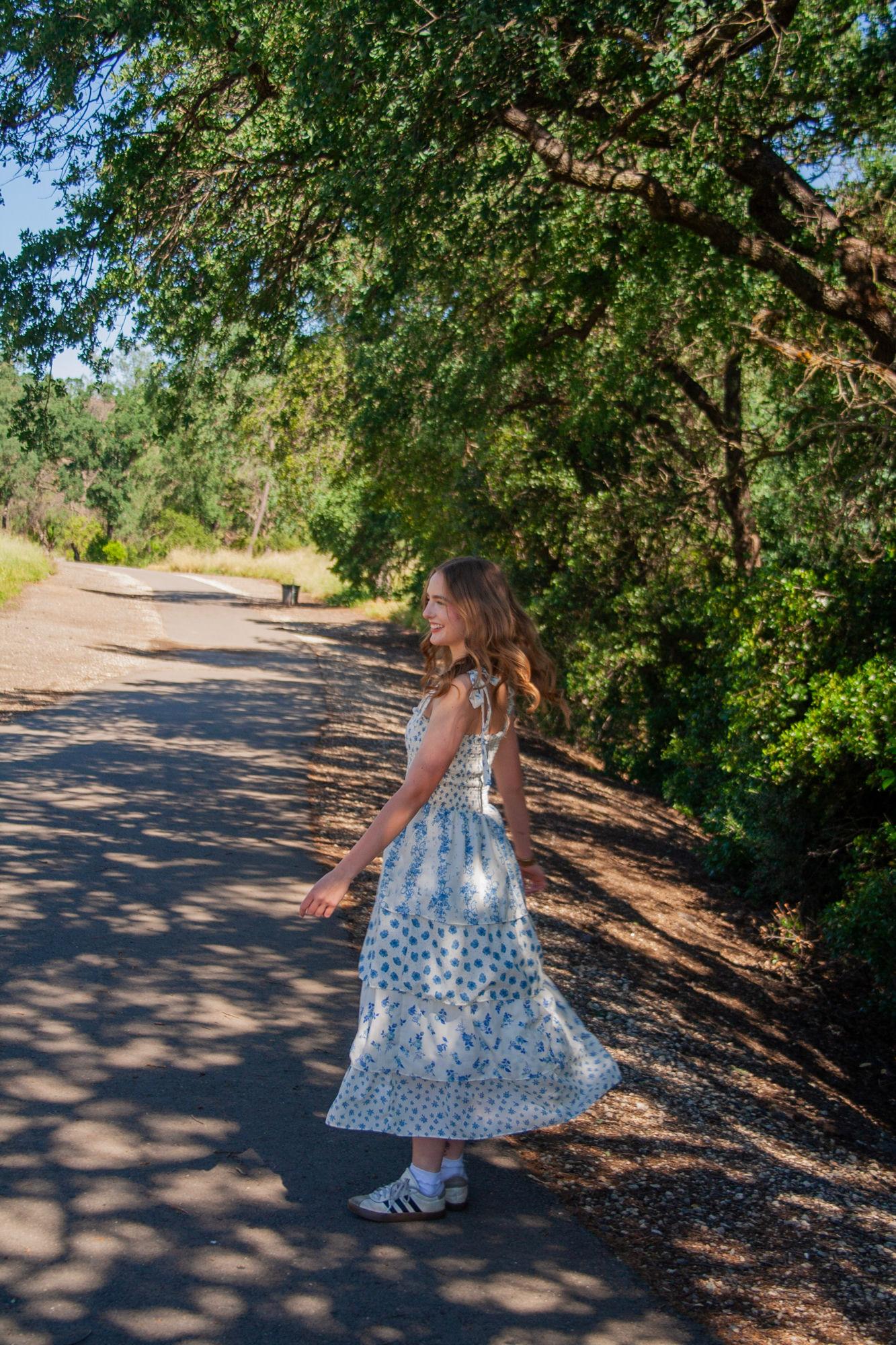 Senior portrait twirling on a tree-lined road in a blue floral dress — Sacramento senior photographer